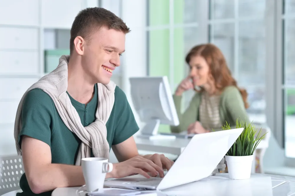 Fiatal munkatárs laptopon dolgozik egy világos irodában